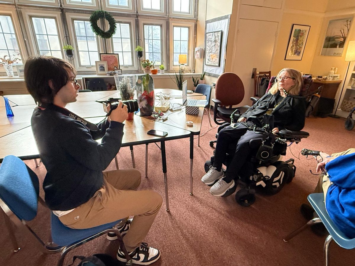 Senior Micah Kramer '26 films an interview with Koniezhny in her room in December 2026. At that point, when she spoke, a microphone on her lapel picked up her voice and broadcast it through a speaker mounted on her wheelchair. Film professor Mydlack plugged the Zoom recorder into the speaker to help the Quill capture the clearest possible sound.