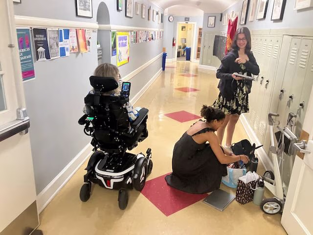 Koniezhny greets seniors Ella West and Louisa Sanchez in spring 2025, in the hallway of the Upper School building outside her classroom.